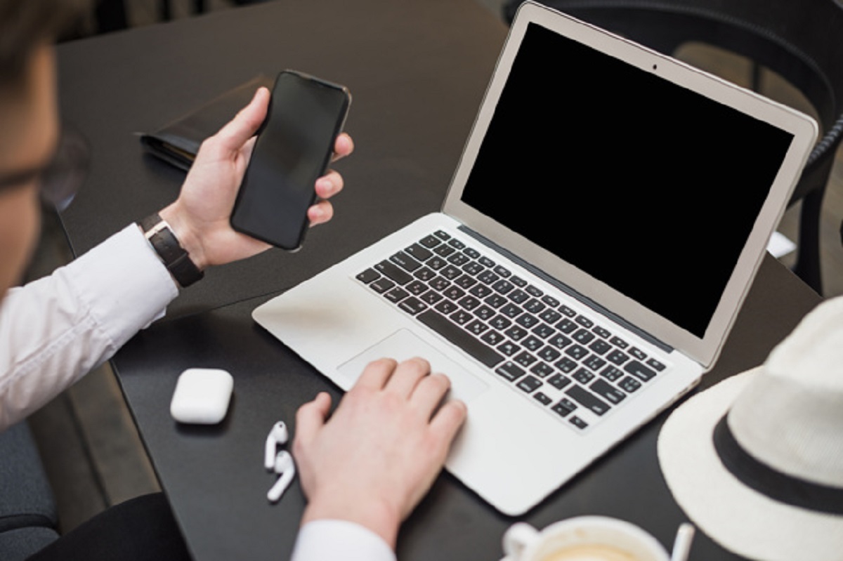 young-businessman-using-laptop-looking-smartphone-screen_23-2148096496